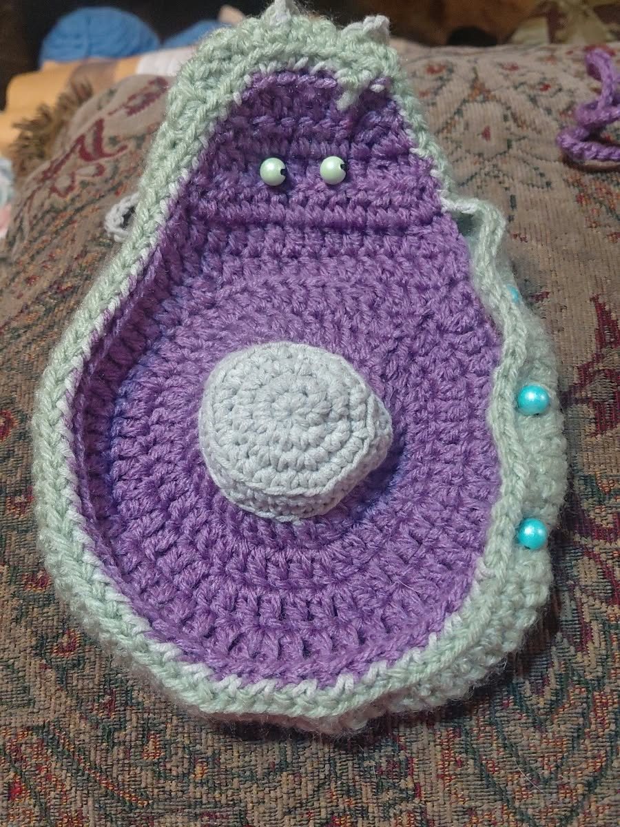 A purple and green crochet pouch shaped like an avocado
