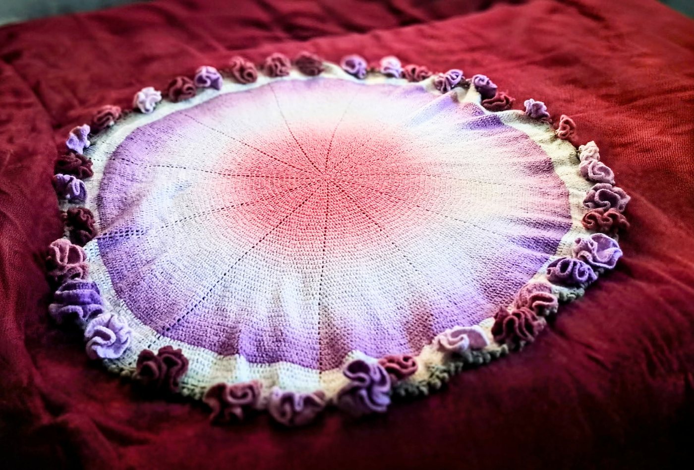 The round rose blanket laid flat on a red bedspread