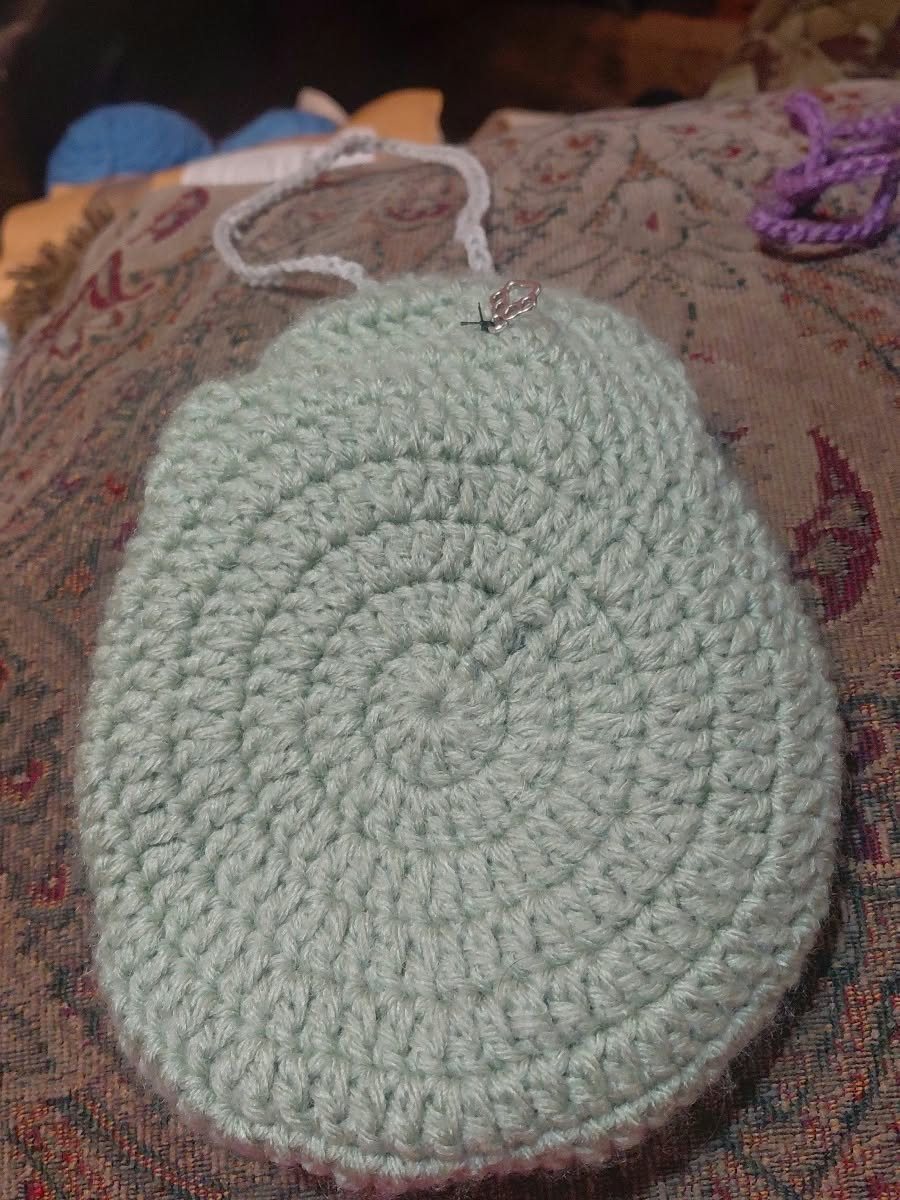 A sage green round crochet bag with a white strap