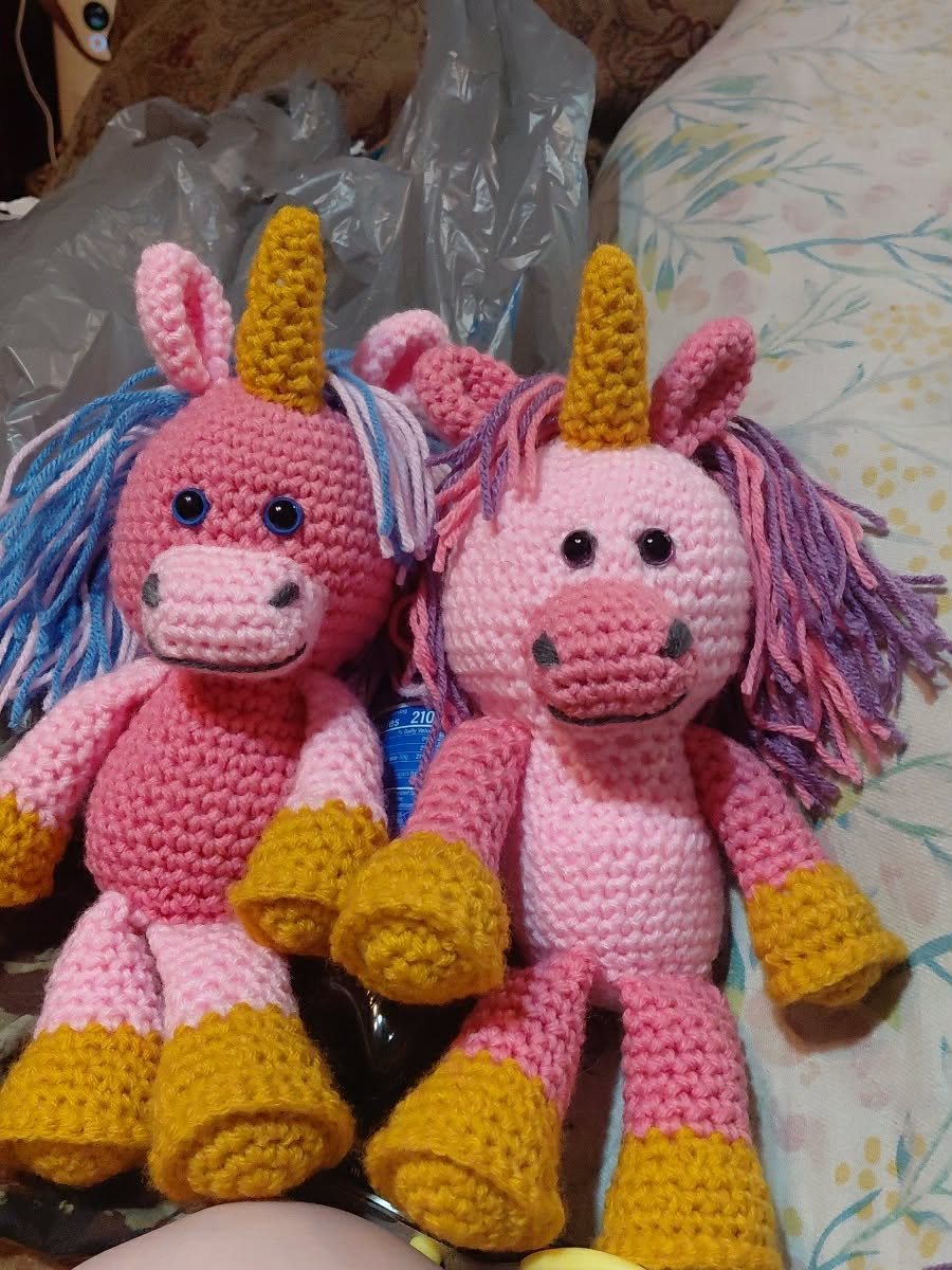 Two pink crochet unicorns with gold horns and hooves